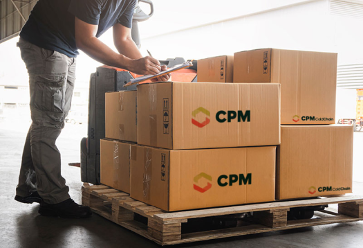 Man with clipboard in a warehouse in front of a pallet of CPM shipping boxes