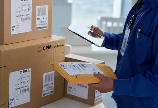 Man in blue uniform with ipad holding a package in front of shipping boxes