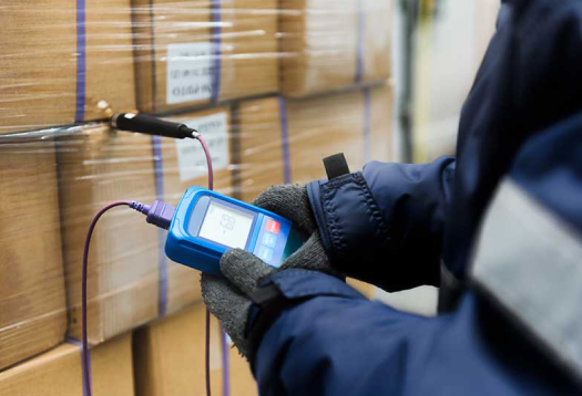 Man in winter coat holding temperature tester in front of cold chain boxes